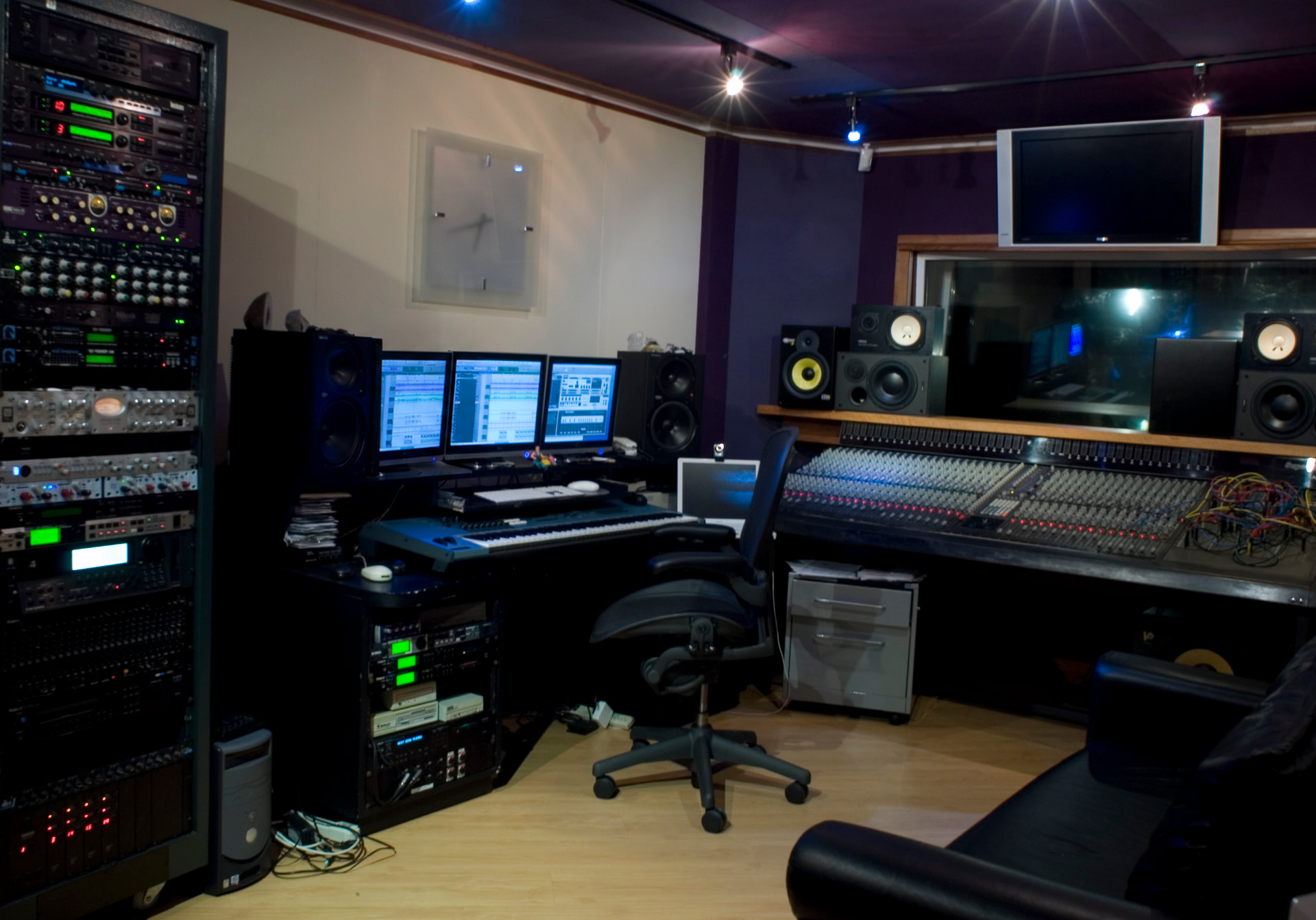 Sala de controle com console analógico, racks de equipamentos e monitores.