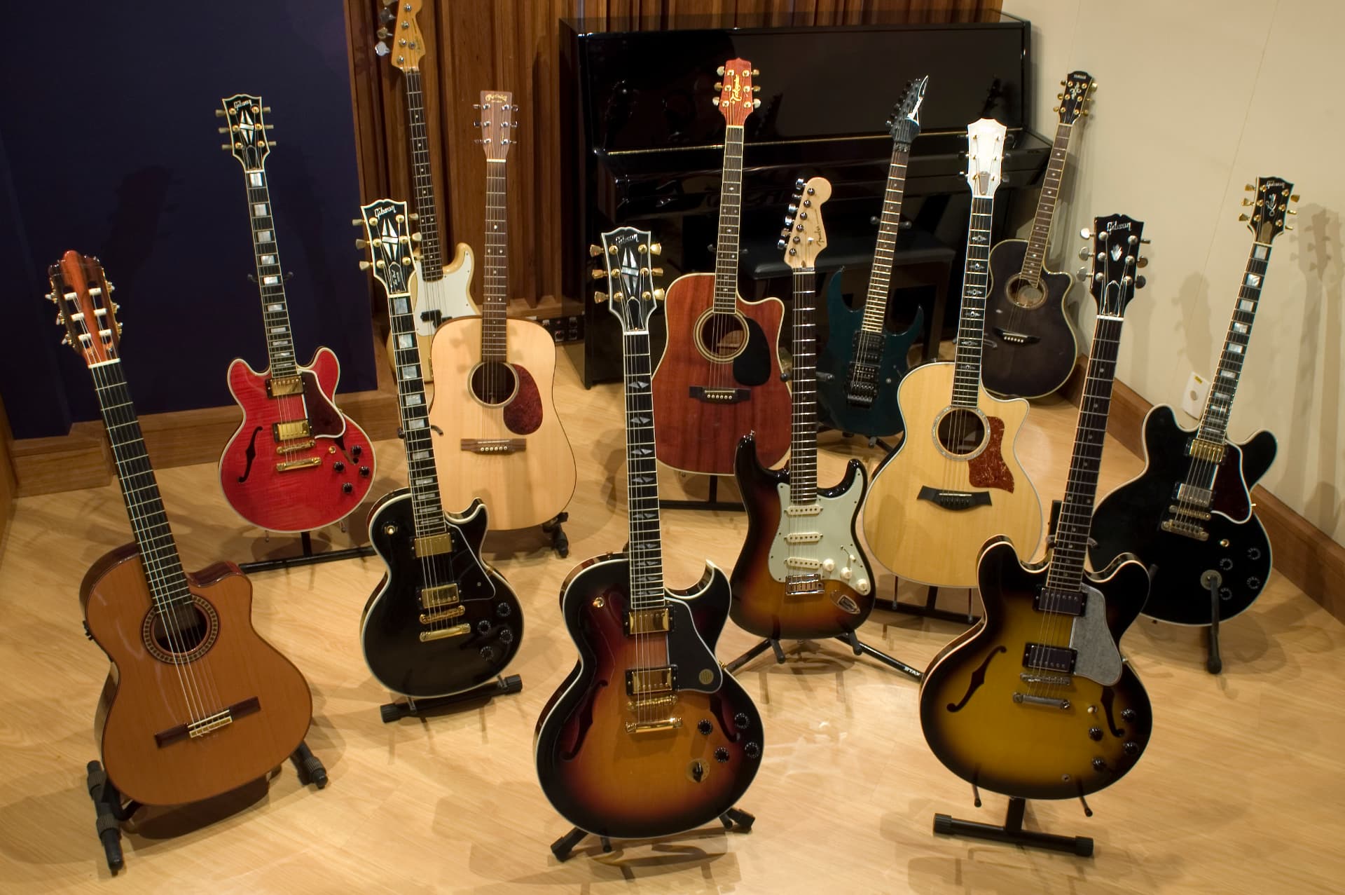 Violões, guitarras e contrabaixos nos cavaletes do estúdio, com o piano Yamaha ao fundo.
